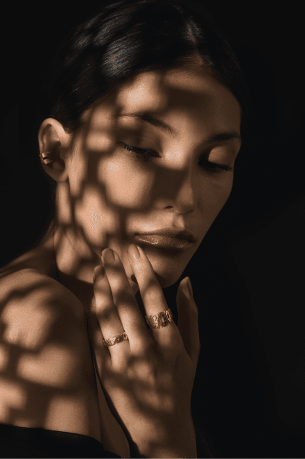 Editorial portrait in dappled light, wearing textured gold rings