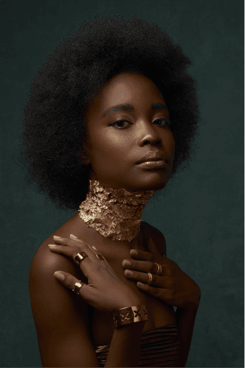 Editorial portrait with a gold-leaf choker, ring and cuff against a green backdrop